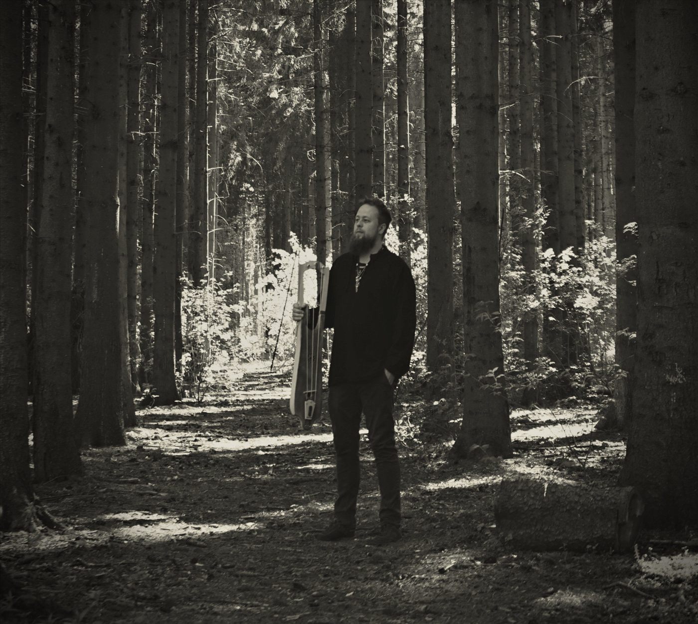 Reidar Schæfer Olsen standing in a pine forest holding a tagelharpa